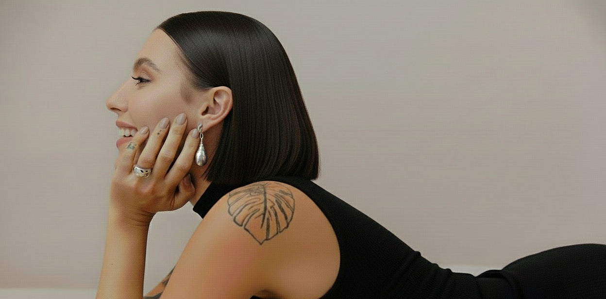 Woman lying on a bed wearing a black strappy top with a tattoo on her shoulder